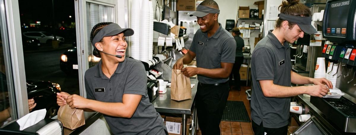A drive-thru crew working a late shift, bagging orders and laughing together