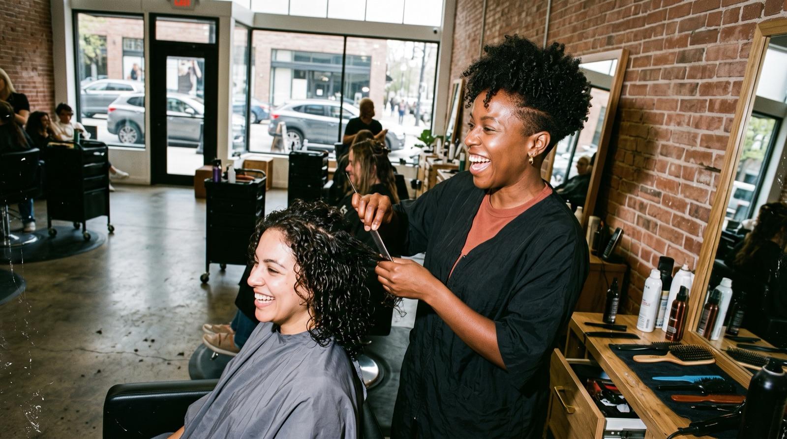 Keisha laughing as she styles a client’s curls at her salon chair